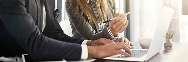 Businessman and business woman sitting at a desk and working alongside each other while looking at a laptop computer.